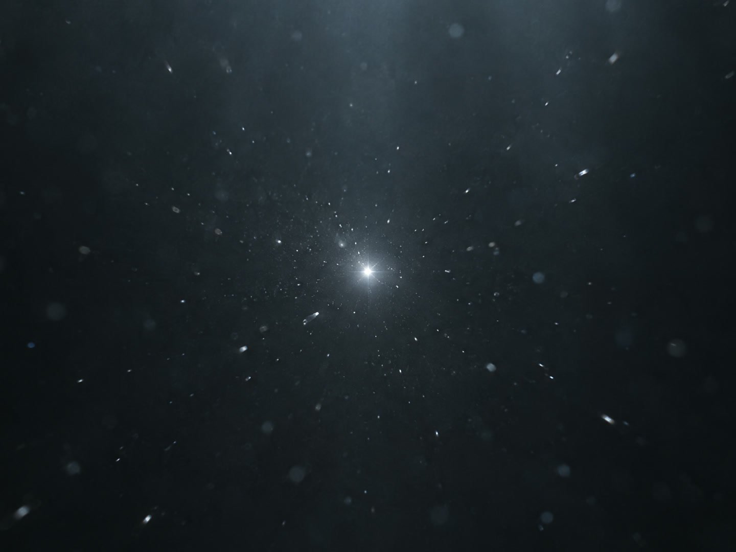 A single point of silver light in the dark, with dust drifting toward it
